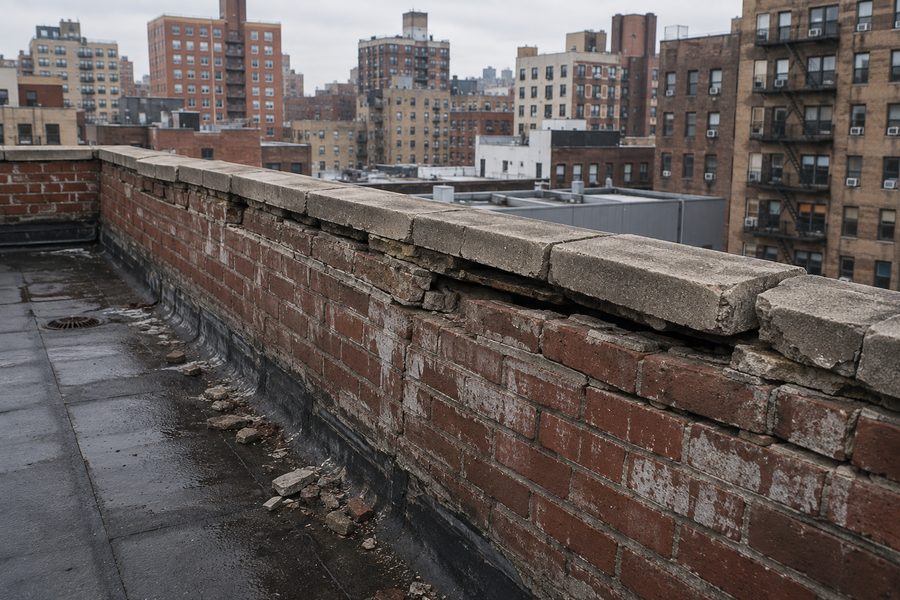 Deteriorated parapet with displaced coping stones above a NYC sidewalk